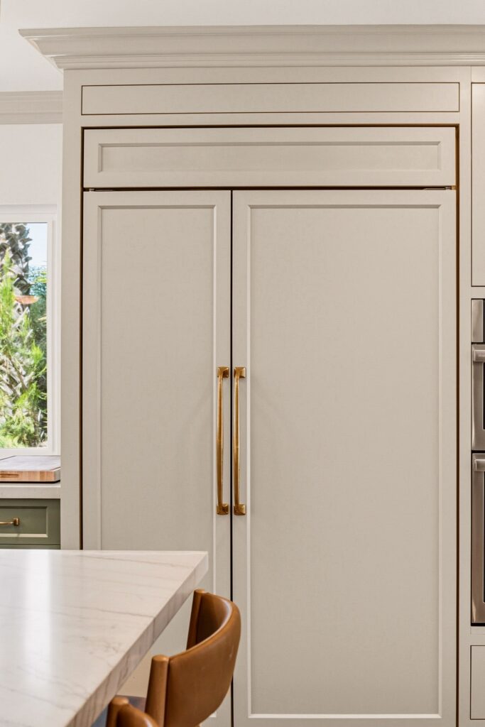 Close-up of a green shaker drawer stack with brass pulls beneath a white veined countertop