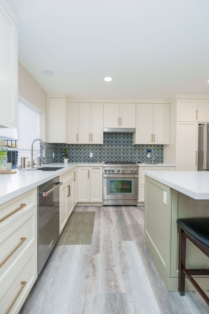 Kitchen sink wall with pull-down faucet, stainless dishwasher, range under hood, cream cabinets and sage green island edge
