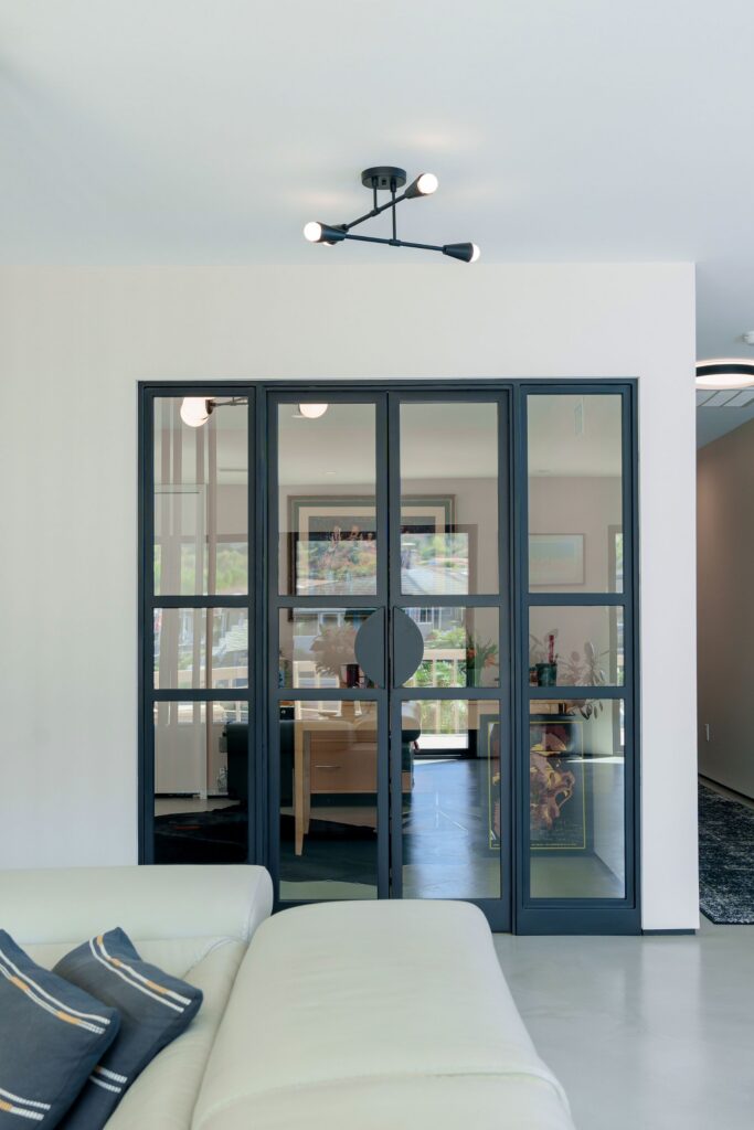 Black steel-framed glass double doors with half-round pulls and sidelights beneath a black semi-flush ceiling light