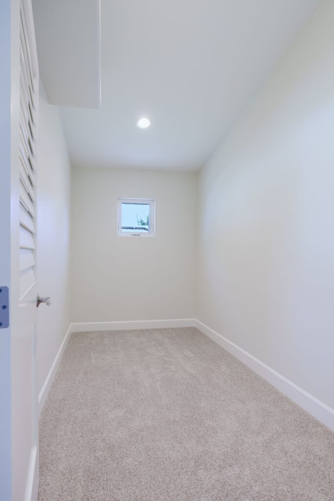 Carpeted walk-in closet with a louvered door, small awning window, recessed light and an overhead shelf
