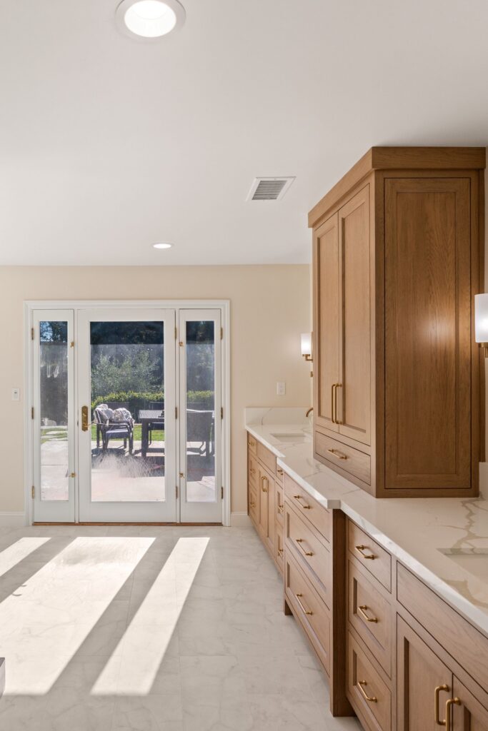 Wood double vanity with tower cabinet and quartz top beside a glass-paneled exterior door with sidelites to the patio