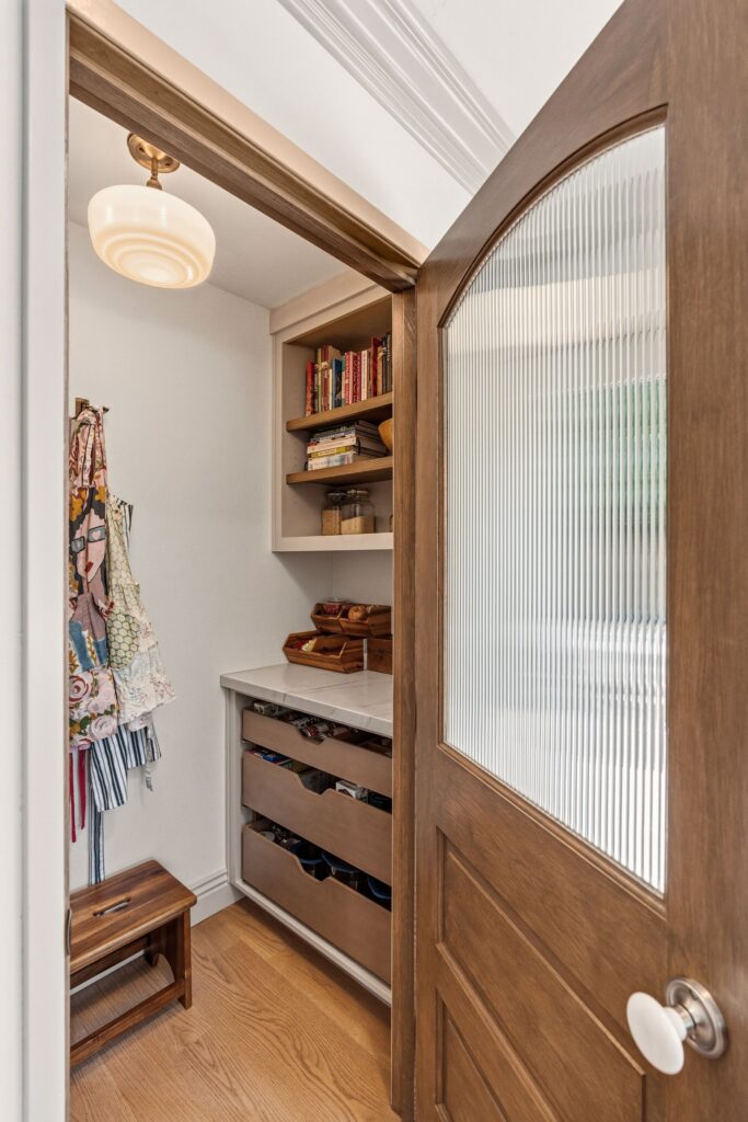 Paneled refrigerator in cream cabinetry with brass pulls and crown molding beside stainless wall ovens