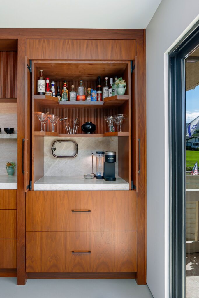 Walnut cabinet with open doors revealing a coffee station, bar shelving, glassware and quartzite backsplash above drawers