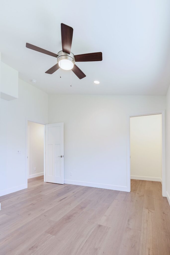 Bedroom with wood-look plank flooring, a ceiling fan, a Shaker-style panel door and an open closet doorway