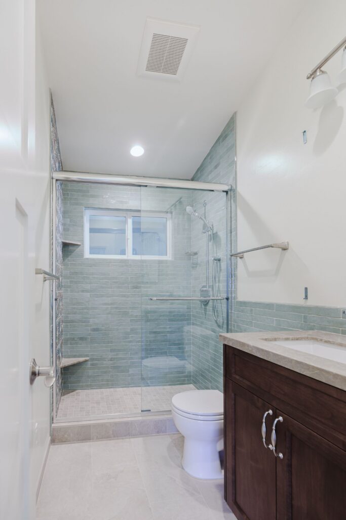 Hall bathroom with a glass-enclosed walk-in shower, green subway tile, a handheld shower and a dark wood vanity