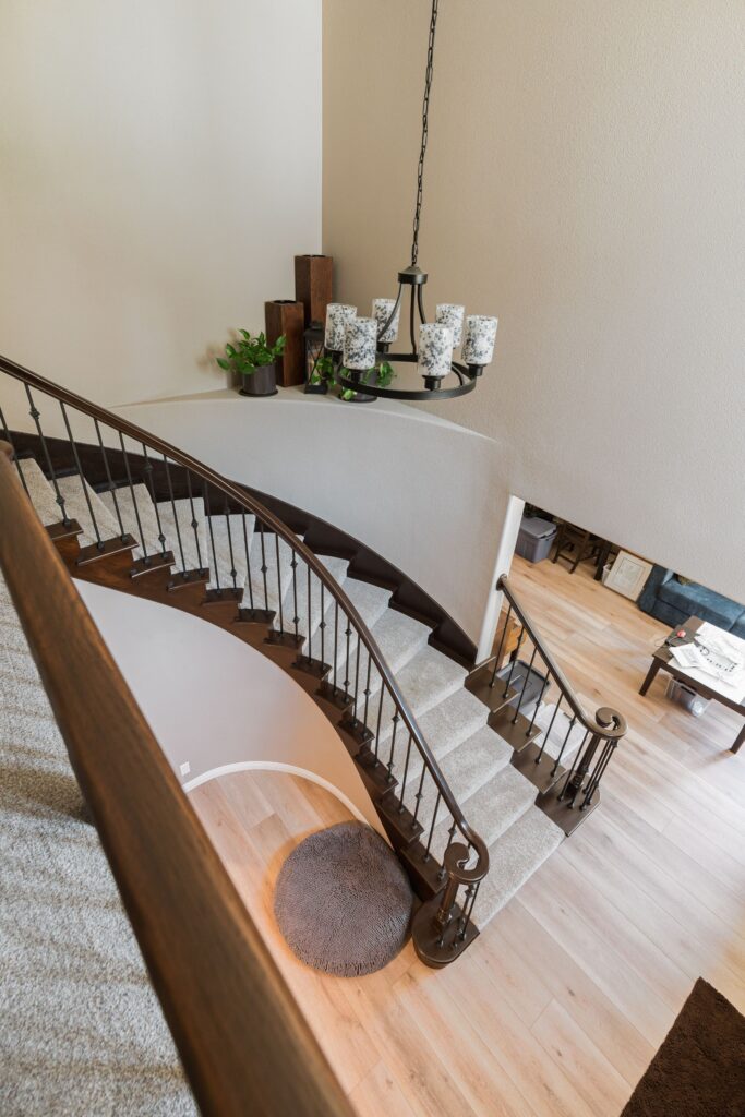 Curved entry staircase with carpeted steps, dark wood handrail, iron balusters, upper landing railing and LVP floor