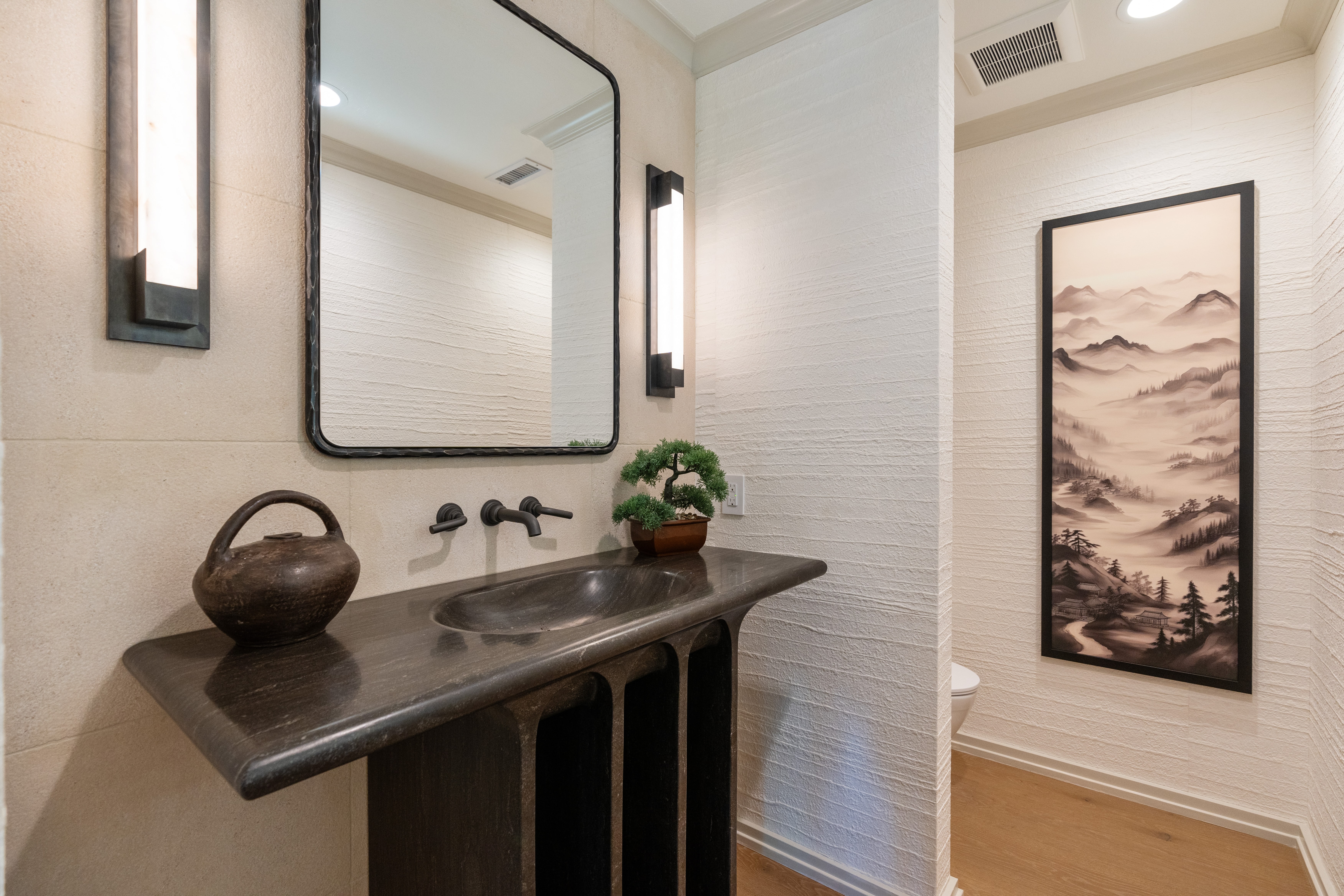 Modern powder room remodel with dark stone floating vanity, vessel-style sink, black-framed mirror, wall sconces, and textured walls.