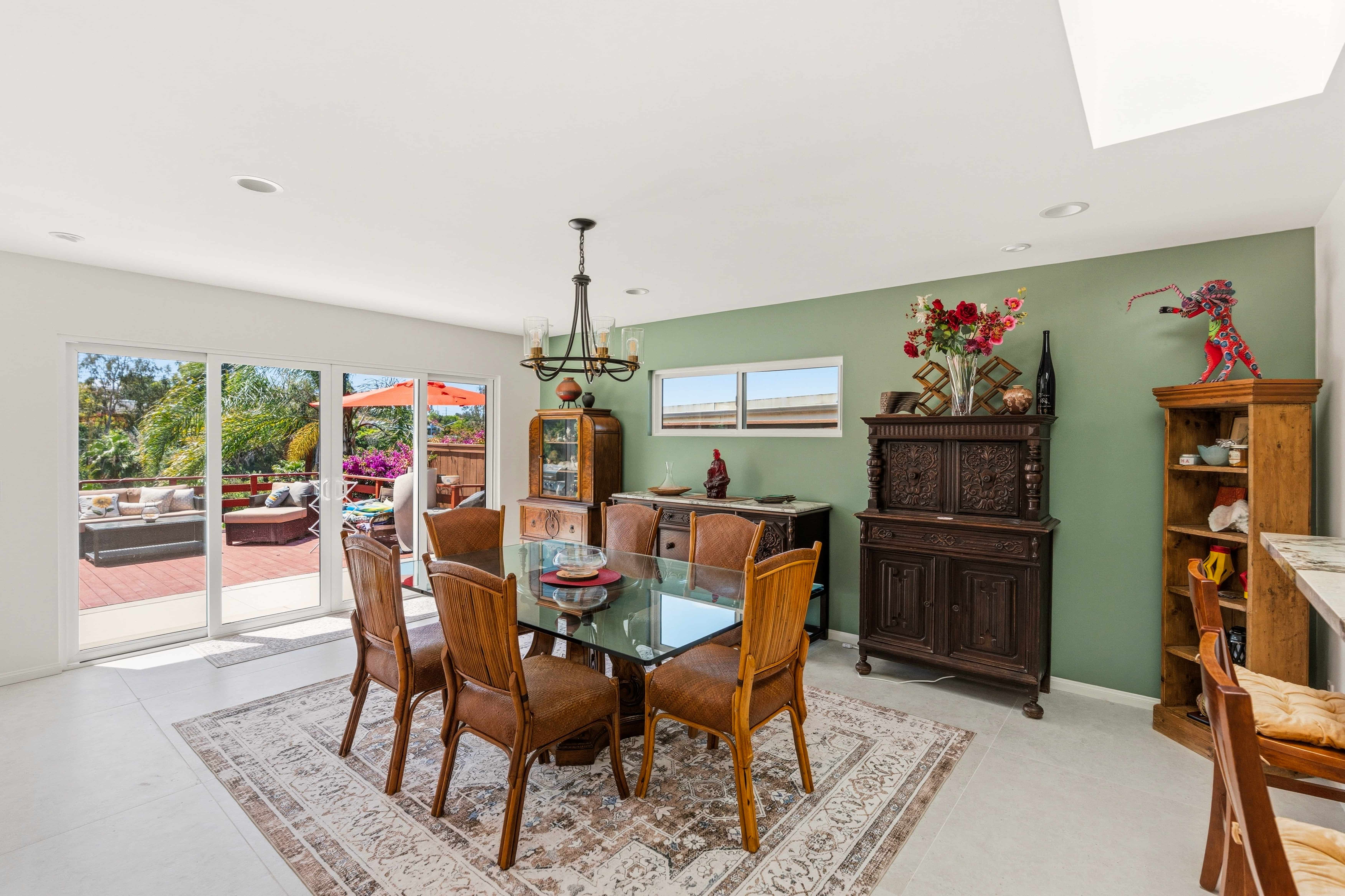 Bright dining room with glass table, wood chairs, and sliding patio doors showing how finished living spaces can enhance a San Diego home.