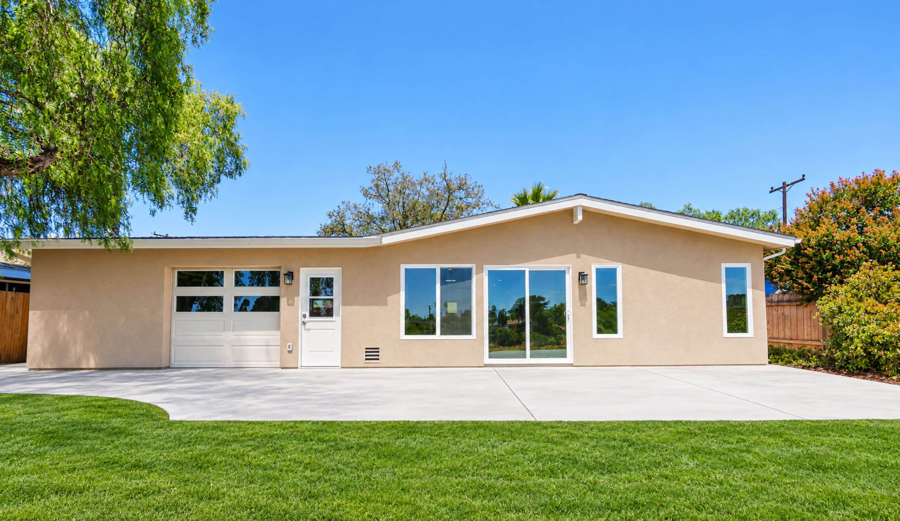 Straight-on view of a remodeled stucco home in with a windowed garage door, entry door, sliding door and a wide concrete patio
