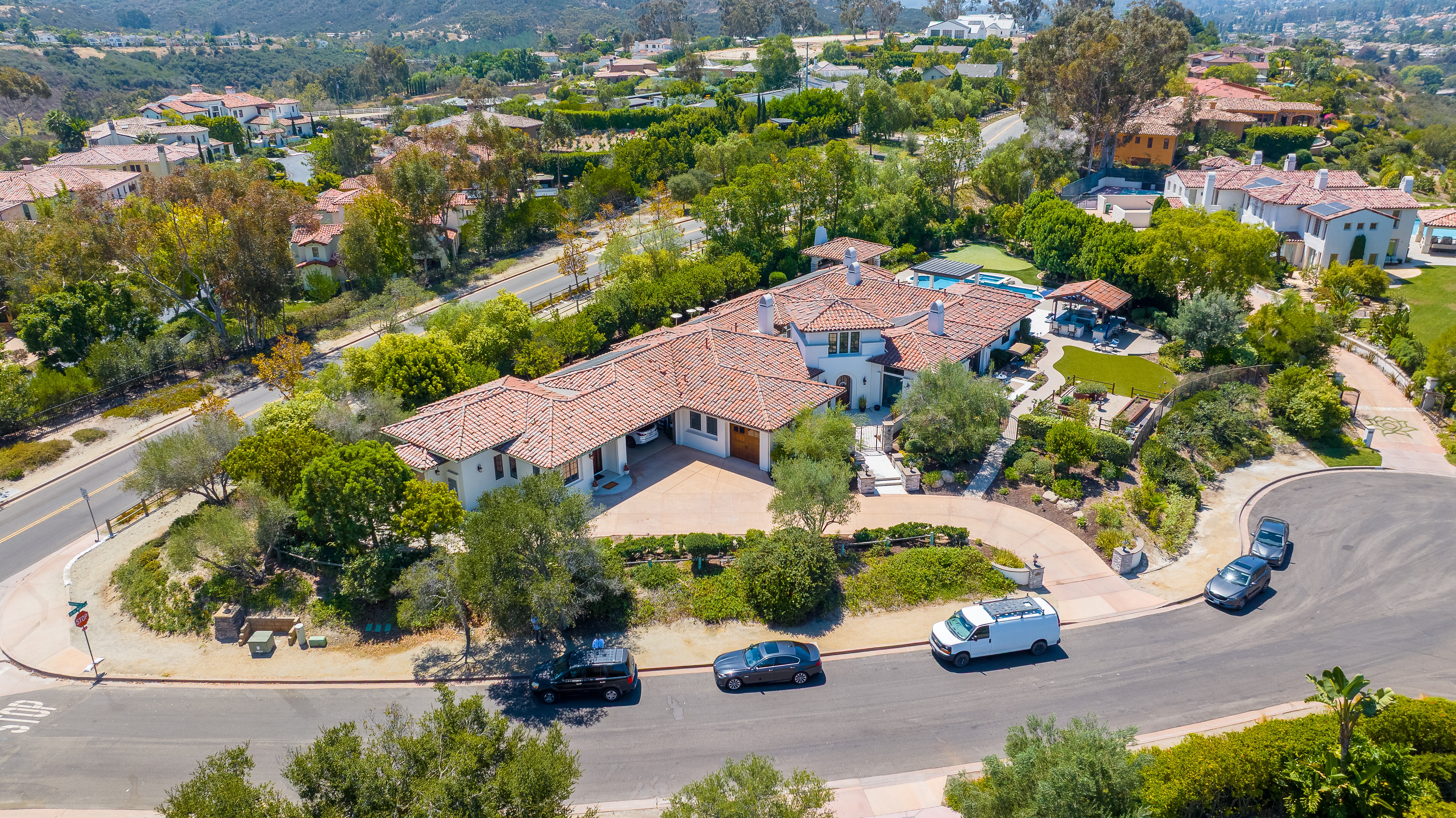 Aerial view of a large San Diego home with an attached garage, tile roof, driveway, and landscaped residential property.
