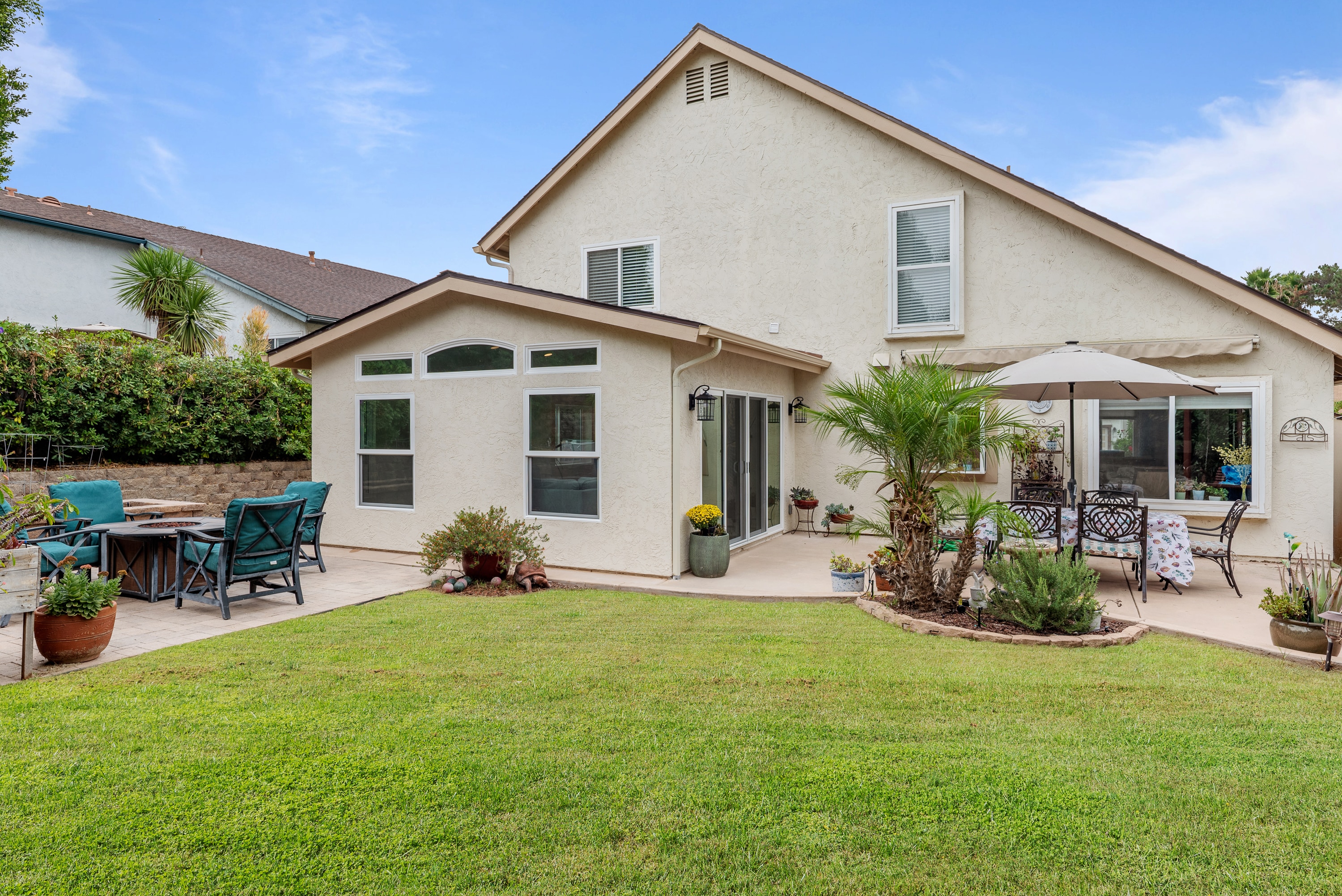 Back of a two-story stucco house with a single-story addition that has a gable roof, arched transom window and sliding glass door, opening onto a patio and lawn.