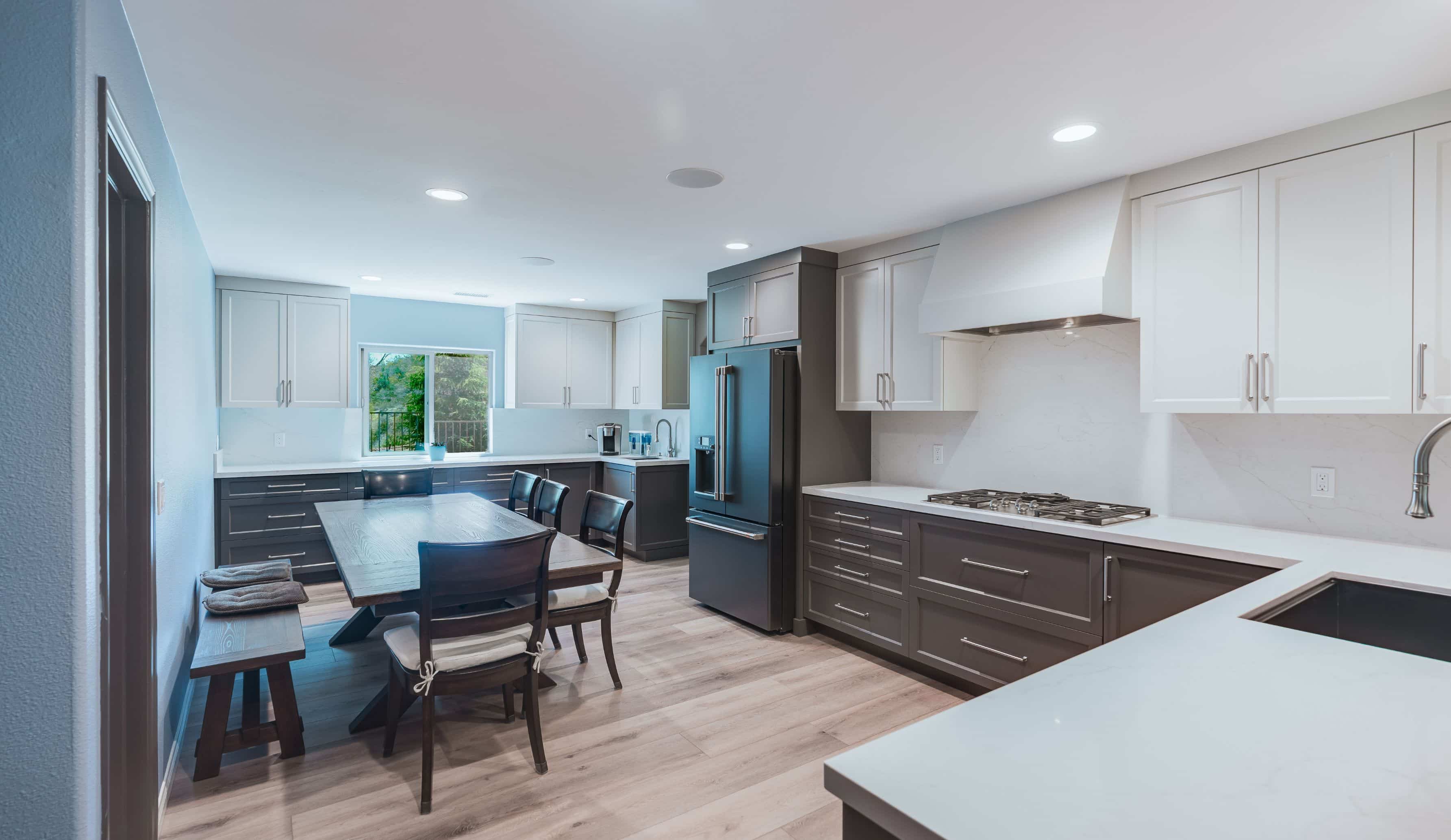 Wide view of a remodeled San Diego kitchen and dining area with a white range hood, gas cooktop, quartz counters and window