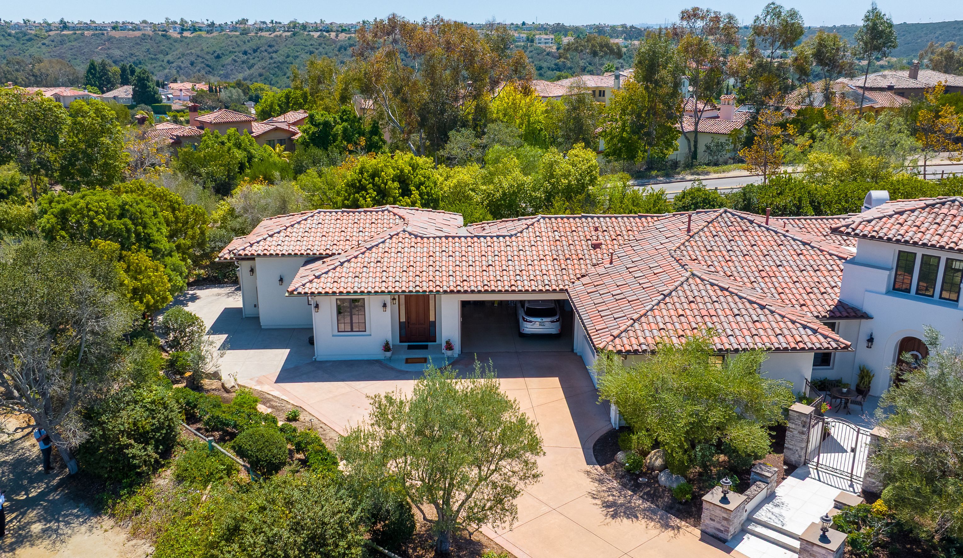 Aerial view of a San Diego home with an attached stucco ADU, red clay tile roofs, a concrete driveway and canyon views beyond