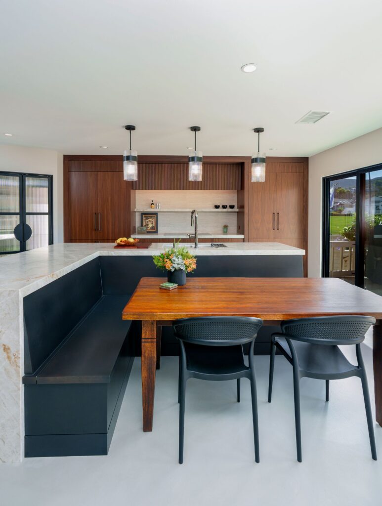 San Marcos kitchen remodel with a built-in black banquette and wood dining table set against a quartzite waterfall island and walnut cabinets