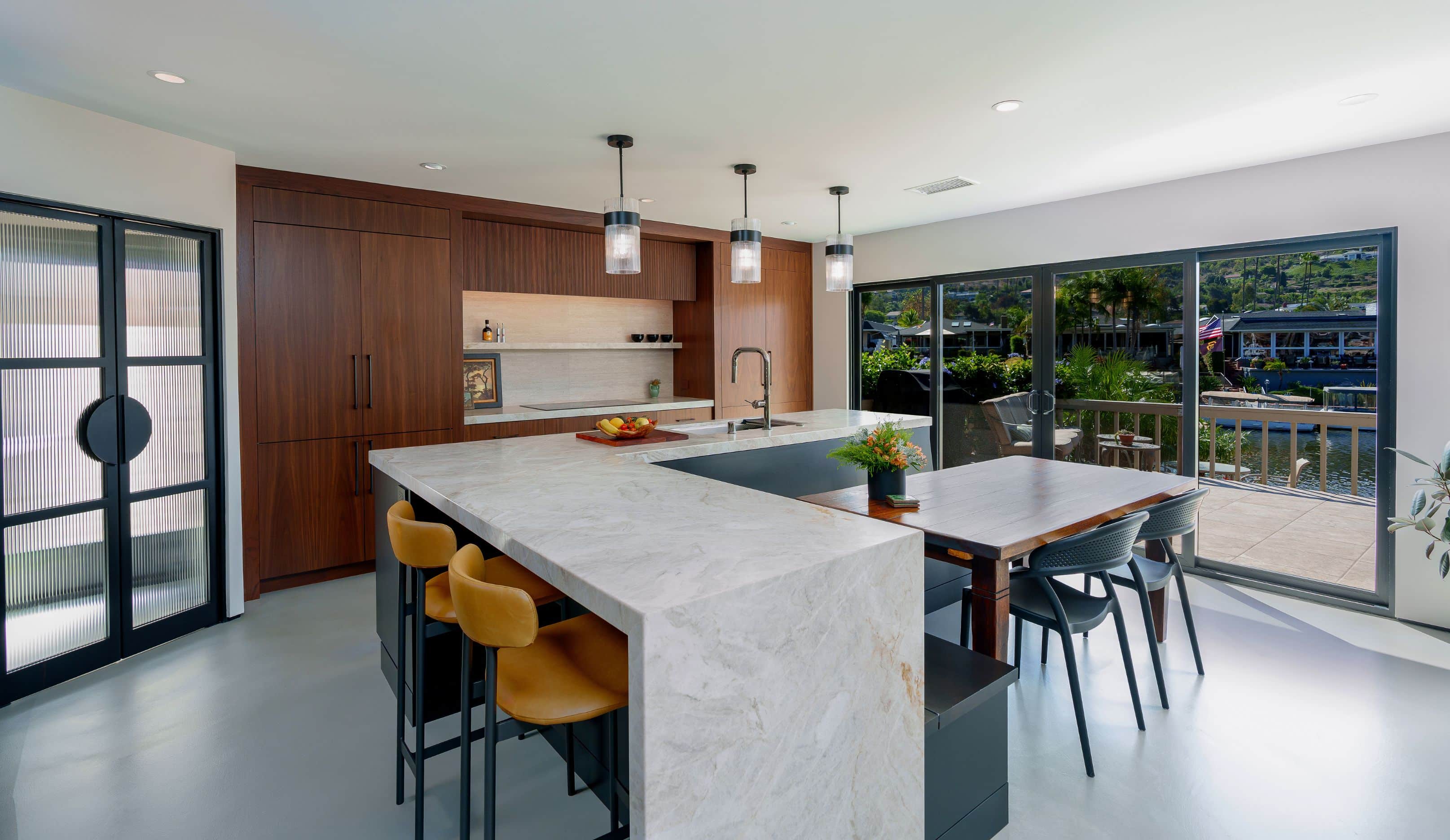 Remodeled San Marcos kitchen with a quartzite waterfall island, leather stools, walnut cabinets and black sliding doors opening to a lakeside deck