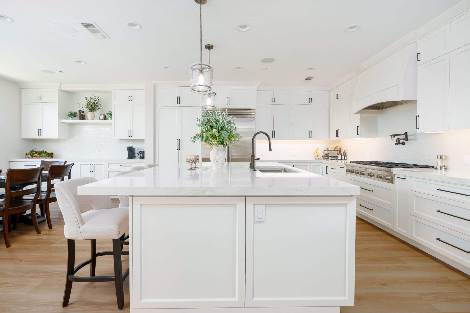 White kitchen island with quartz countertop and sink, professional rangetop with pot filler, cabinetry hood, and coffee station with floating shelves.